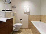 Moderne badeværelse med væghængt toilet, hvidt badekar, træskabe, klinkegulv og -vægge samt to hvide håndklæder på væggen.