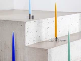Fire farverige stearinlys - blå, lyseblå, gul og lysegrøn - står i moderne metalholdere på betontrin med en minimal, moderne baggrund.