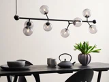 Et moderne spisebord med sorte stole, minimalistisk service, en tekande, en vase med hvide tulipaner og en moderne lysekrone med runde glaspærer.