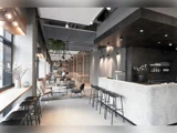 Moderne minimalistisk caféindretning med betonbar, sorte taburetter, loungestole, store vinduer og blød belysning. Dekorative planter og neutrale toner skaber en elegant og indbydende atmosfære.