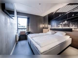 Et moderne hotelværelse med en stor seng, hvidt sengetøj, et væghængt tv, et skrivebord ved vinduet og mørke vægge med et vægmaleri med industrielt tema over sengen.