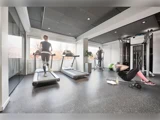 Tre personer træner i et lyst fitnesscenter: en på løbebånd, en på crosstrainer og en, der laver sit-ups med en grøn bold. Træningsudstyr og vandflaske er synlige.