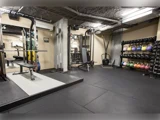 Et veludstyret fitnesscenter med vægtstativer, kettlebells, bænkpres, modstandsmaskiner og træningsudstyr på sort gummigulv.