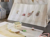 Et legeområde med et stribet stofpanel med frugt- og grøntsagslegetøj i gennemsigtige lommer, en legetøjskurv og et tæppe med et stort bananmotiv og små legetøjsfødevarer.