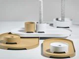 Minimalistiske guld- og hvide bakker og cylindriske holdere, hvoraf nogle bærer teksturerede hvide lys, arrangeret på en lys overflade.
