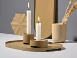 To tændte hvide stearinlys på en moderne beige bakke med en beige kop med tørret græs og geometriske dekorationsgenstande i en minimalistisk indretning.