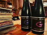 To flasker Ghost Brewing Purple Moon Imperial Stout på et træbord ved siden af en stak vinylplader i en hyggelig, svagt oplyst bar.