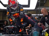 En Formel 1-kører i Red Bull-dragt stiger ind i en bil i garagen, hjulpet af teammedlemmer i sorte uniformer.