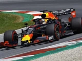 En Red Bull Racing Formel 1-bil kører rundt om et hjørne på en racerbane, mens føreren har hjelm på, og farverige sponsorlogoer er synlige på bilen.
