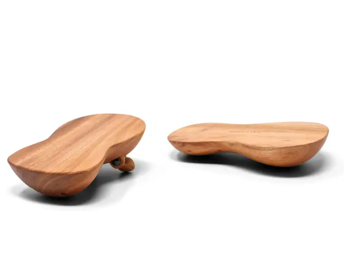 To glatte, jordnøddeformede massageredskaber af træ vises på en hvid baggrund; det ene hviler på siden, det andet på den flade overflade.