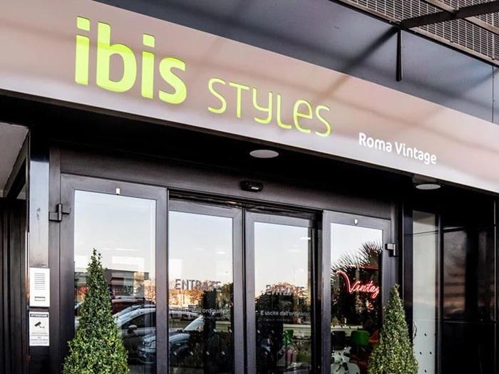 Indgang til Ibis Styles Roma Vintage hotel med glasdøre, to potteplanter og hotellets navn over indgangen.