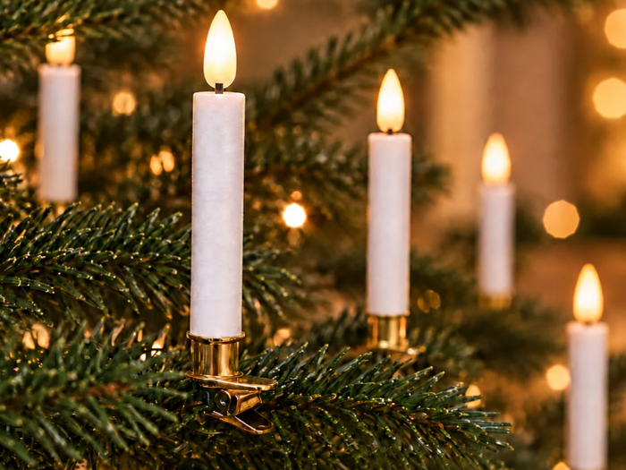 Hvide elektriske stearinlys, der er fastgjort til grenene på et juletræ, og som lyser op mod en sløret baggrund af lys.