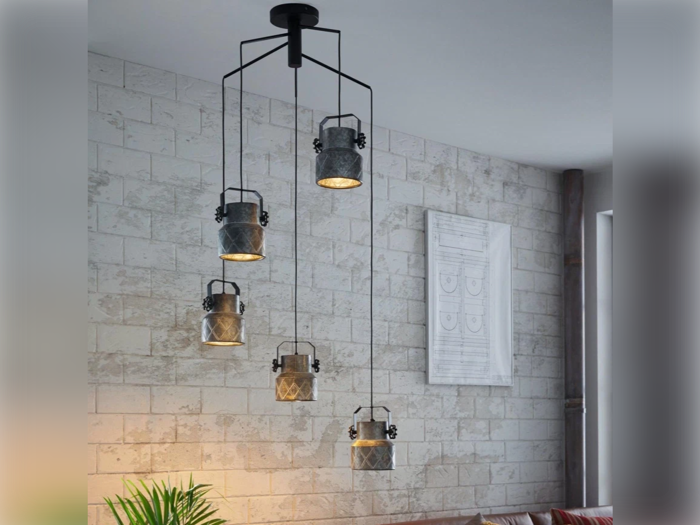 Et moderne loftsarmatur med fem hængende lamper i lanternestil i en stue med en hvid struktureret murstensvæg.