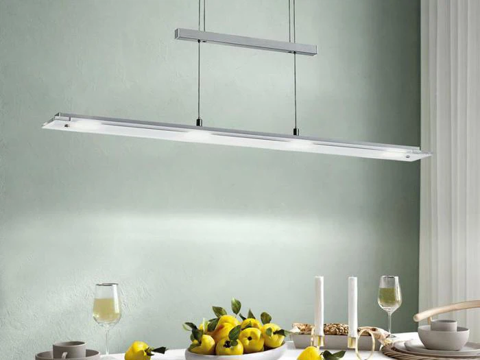 En moderne rektangulær pendel hænger over et hvidt spisebord dækket med citroner, vinglas, lysestager og tallerkener mod en lysegrøn væg.