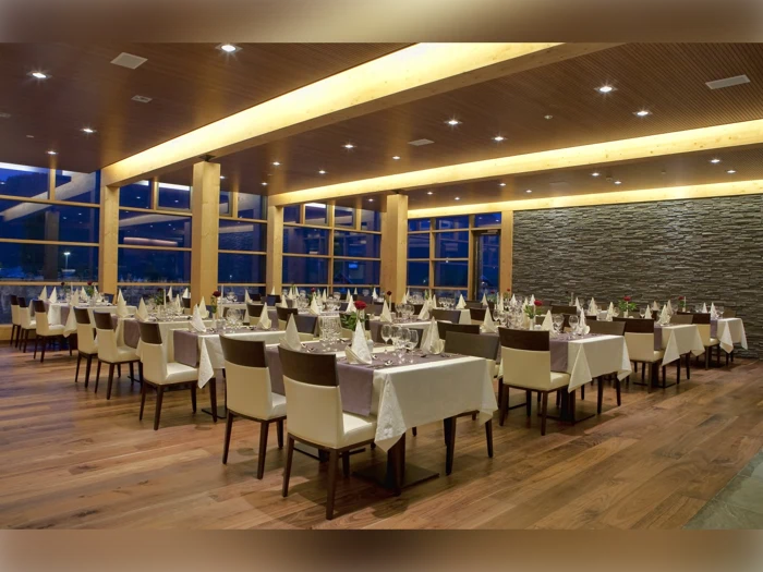 Rummelig, moderne restaurant med trægulve, store vinduer og pænt dækkede borde med hvide duge og foldede servietter, klar til gæster.