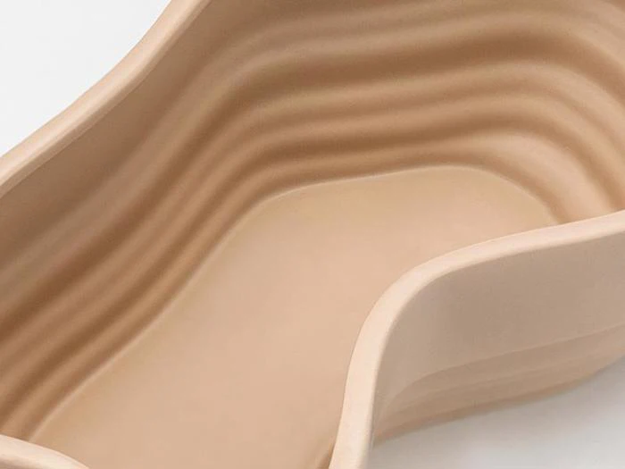 Nærbillede af en glat, beige, lagdelt keramikgenstand med bølgende kurver og en bølget, organisk form.