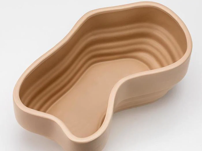 En beige, nyreformet keramikskål med glatte, lagdelte riller langs de indvendige sider på en hvid baggrund.