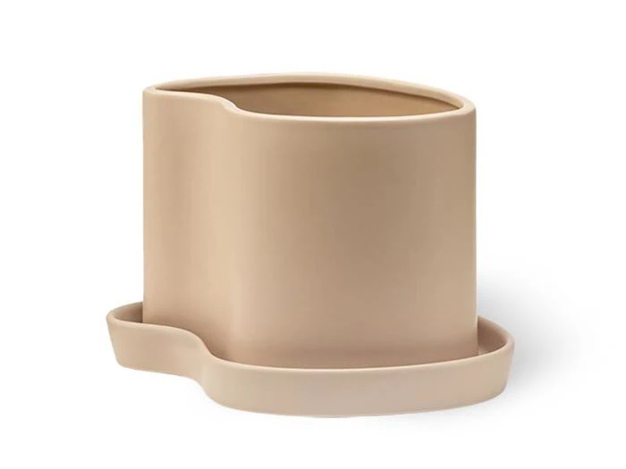En beige, asymmetrisk urtepotte med en matchende uregelmæssig underkop, begge i glat materiale, vist på en hvid baggrund.