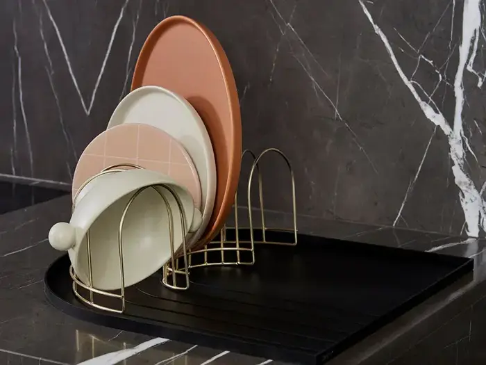 Et opvaskestativ rummer flere tallerkener og skåle i forskellige størrelser og farver på en sort bordplade med en mørk marmorbagside.