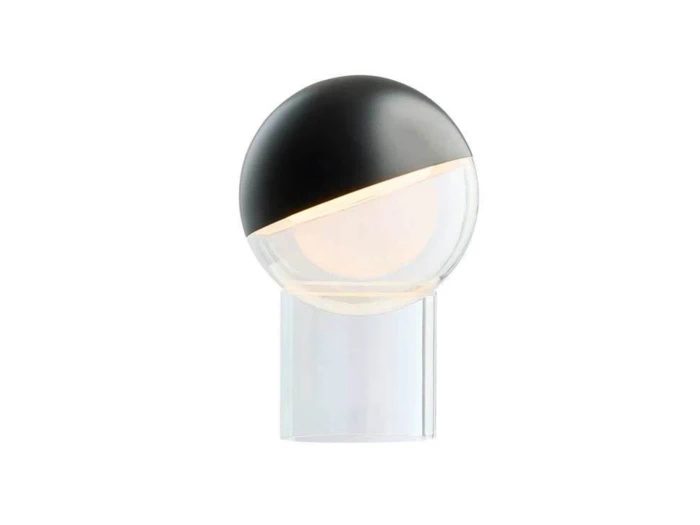 En moderne bordlampe med en gennemsigtig, cylindrisk fod og en rund glasskærm, der delvist er dækket af en sort kappe, og hvor lyset stråler ud fra det synlige område.