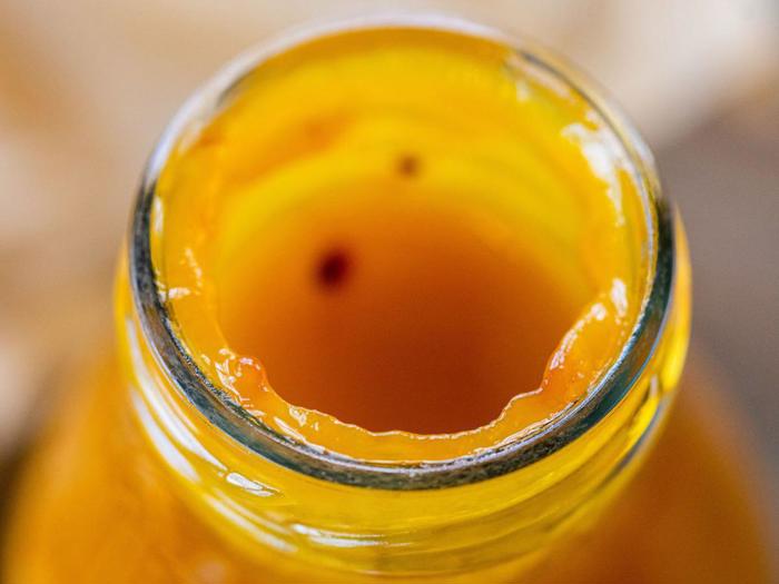 Nærbillede af mundingen på en glasflaske fyldt med tyk, gul-orange væske, muligvis juice eller sauce, med rester rundt om kanten.
