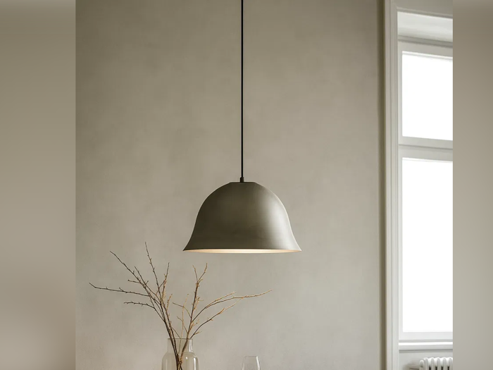 En moderne kuppelformet pendel hænger fra loftet over et bord med en glasvase med nøgne grene, der står op ad en lys væg og et vindue.