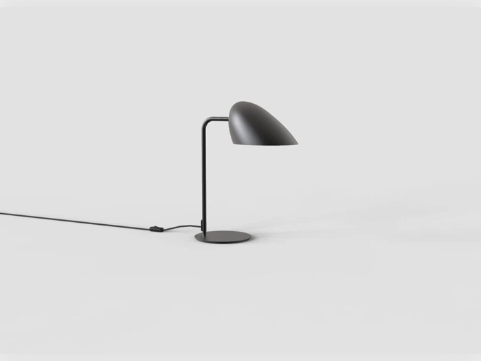 En moderne sort bordlampe med en buet lampeskærm og et slankt stativ står på en hvid overflade, mens ledningen og afbryderen hænger bagved.