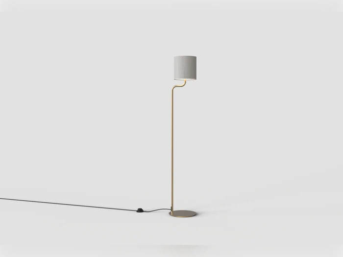 Minimalistisk gulvlampe med et tyndt, guldfarvet stativ og en cylindrisk lampeskærm.