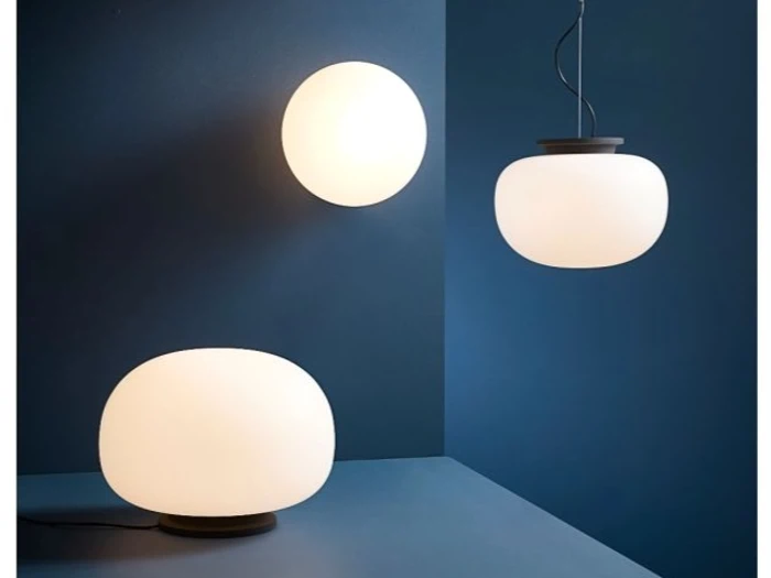 Tre moderne hvide kuglelamper – en væglampe, en bordlampe og en pendel – er udstillet foran en blå væg og en blå overflade.