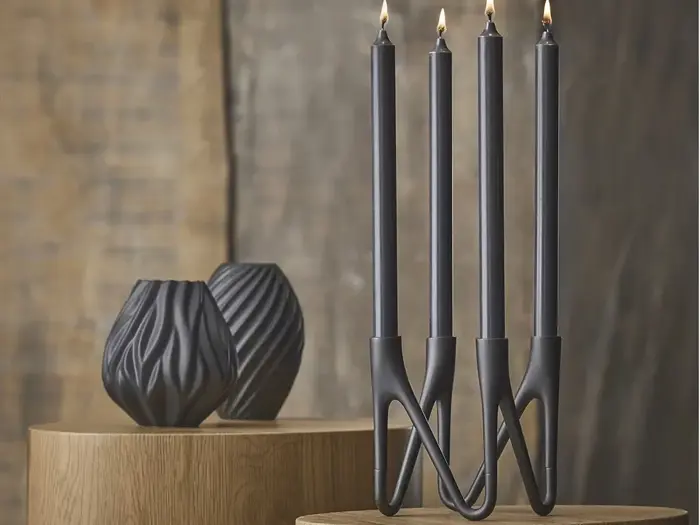 Fire sorte lys i en moderne, sammenhængende holder er tændt på en træoverflade med to sorte vaser med struktur i baggrunden.