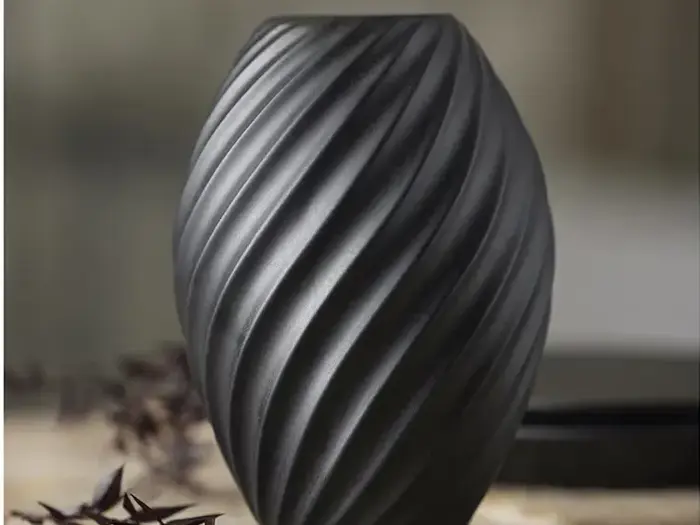 En matsort vase med et snoet spiraldesign står på en sløret, neutral baggrund.