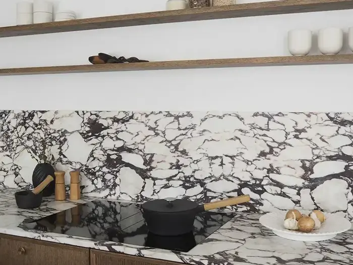 Moderne køkken med bordplade og stænkplade i sort og hvid marmor, åbne træhylder med service og en sort gryde på komfuret.