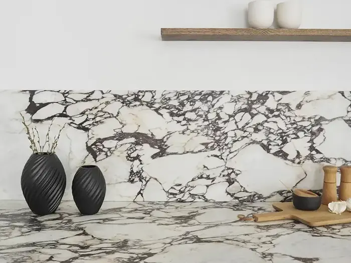 En køkkenbordplade i marmor med sorte og hvide årer, sorte vaser, et skærebræt i træ, krydderibeholdere og to hvide kopper på en svævende hylde ovenover.