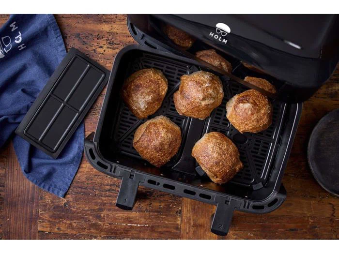 Seks gyldenbrune rundstykker i en friturekurv, med et blåt klæde og en rektangulær sort bakke på et træbord i nærheden.