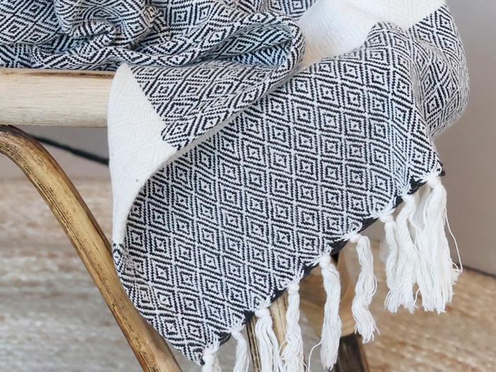 Et vævet tæppe med et sort og hvidt diamantmønster og frynsede kanter draperet over siden på en træstol.