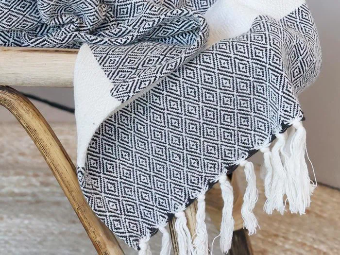 Et vævet tæppe med et sort og hvidt diamantmønster og frynsede kanter draperet over siden på en træstol.