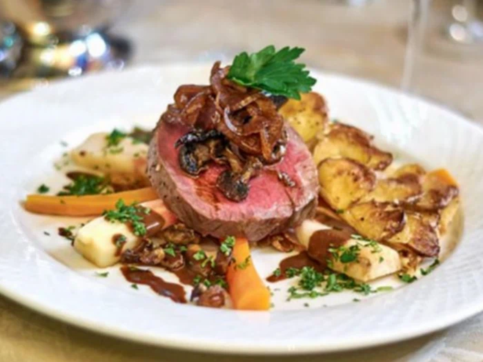 En gourmetret med en mediumstegt bøf toppet med karamelliserede løg og persille, serveret med ristede kartofler, gulerødder og pastinak og pyntet med hakkede krydderurter.