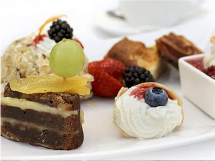 En tallerken med forskellige desserter, herunder lagkage, flødeskumskager toppet med frugt, bær og en skål med rød sauce, på en hvid dug.