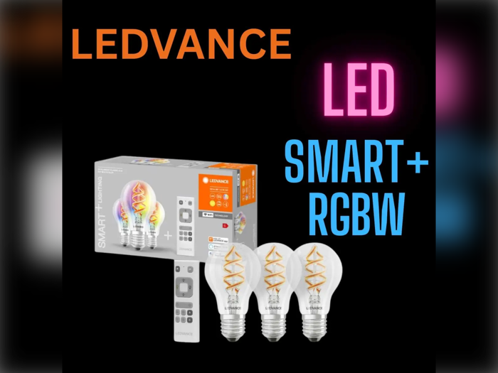 En æske med LEDVANCE Smart+ RGBW LED-pærer med tre pærer og en fjernbetjening vist på en sort baggrund med farverig tekst.