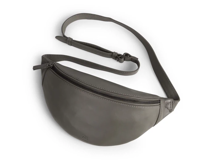 En grå crossbody-bæltetaske i læder med justerbar rem og en forlomme med lynlås, vist på en hvid baggrund.