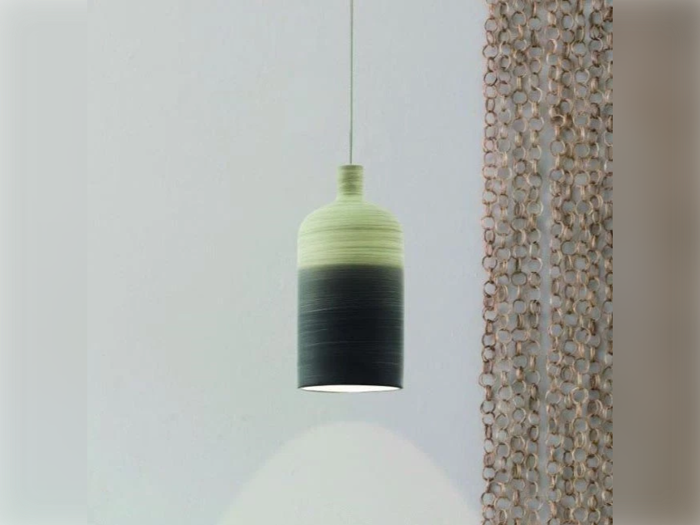 En moderne, cylindrisk pendellampe med en gradient fra lys til mørk, der hænger ved siden af et dekorativt perlegardin mod en almindelig væg.