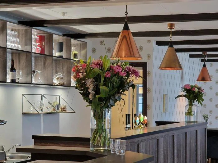 Moderne barindretning med trædetaljer, store vaser med pink og grønne blomster på disken, glas på hylder og varme pendler, der hænger ned fra loftet.