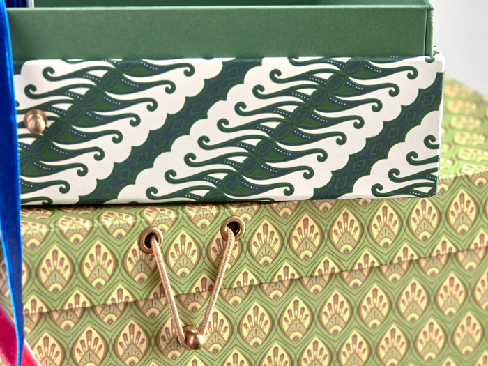 To dekorative æsker med grønne mønstre; den øverste æske har et bølget design, og den nederste har et bladlignende mønster med guldsnorlukninger.