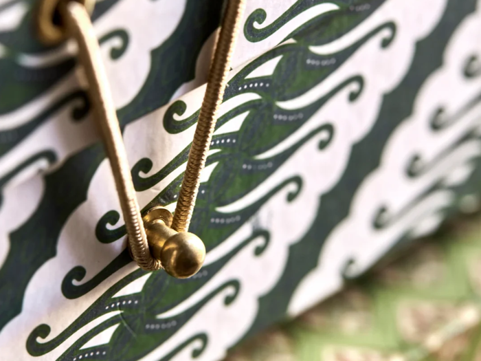 Nærbillede af en mønstret stofpose med grønne og hvide bølgemønstre og guldfarvet håndtagsbeslag i forgrunden.