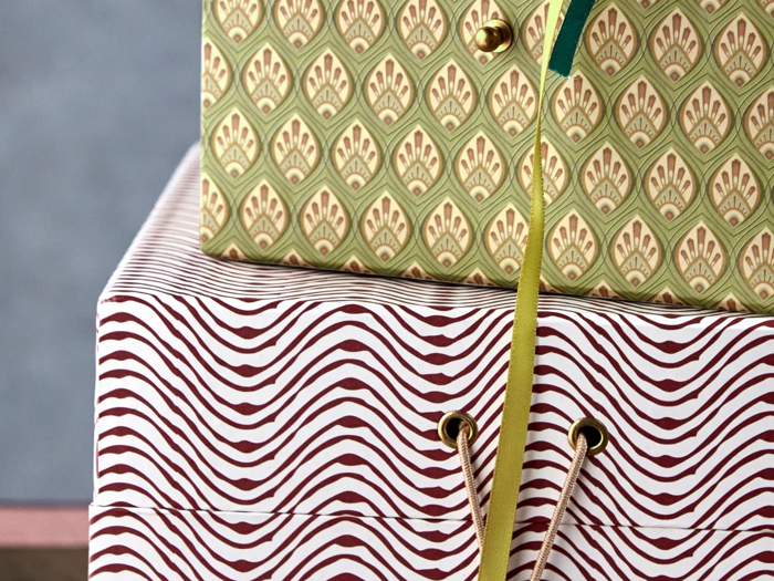To gaveæsker er stablet. Den øverste æske har et grønt og gyldent mønster med et gult bånd, og den nederste æske har et rødt og hvidt bølgestribet design.