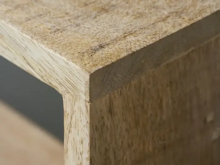 Nærbillede af hjørnet af et træbord eller en hylde, der viser det lyse træs naturlige årer og struktur.