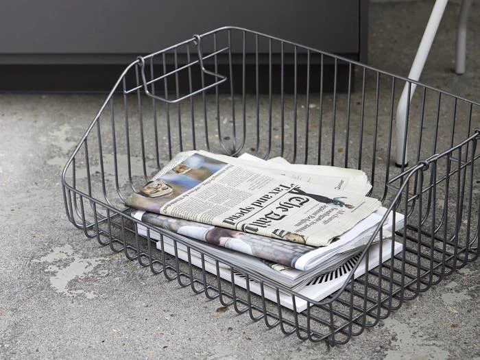 En trådkurv på et betongulv indeholder foldede aviser og magasiner.