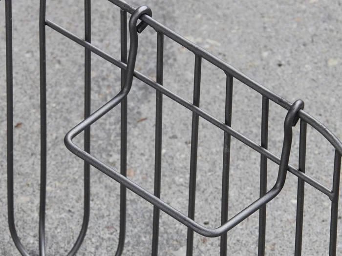 Nærbillede af et metalcykelstativ med rektangulære og lodrette stænger, vist mod en ru betonoverflade.