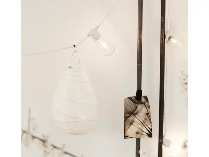 En hvid papirlygte og et sort-hvidt foto hænger i snore med lyskæder op ad en hvid væg.
