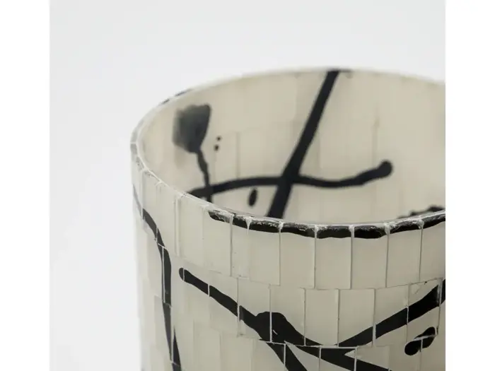 Nærbillede af en cylindrisk hvid vase med kakkelstruktur og abstrakte sorte streger og stænk som dekoration.